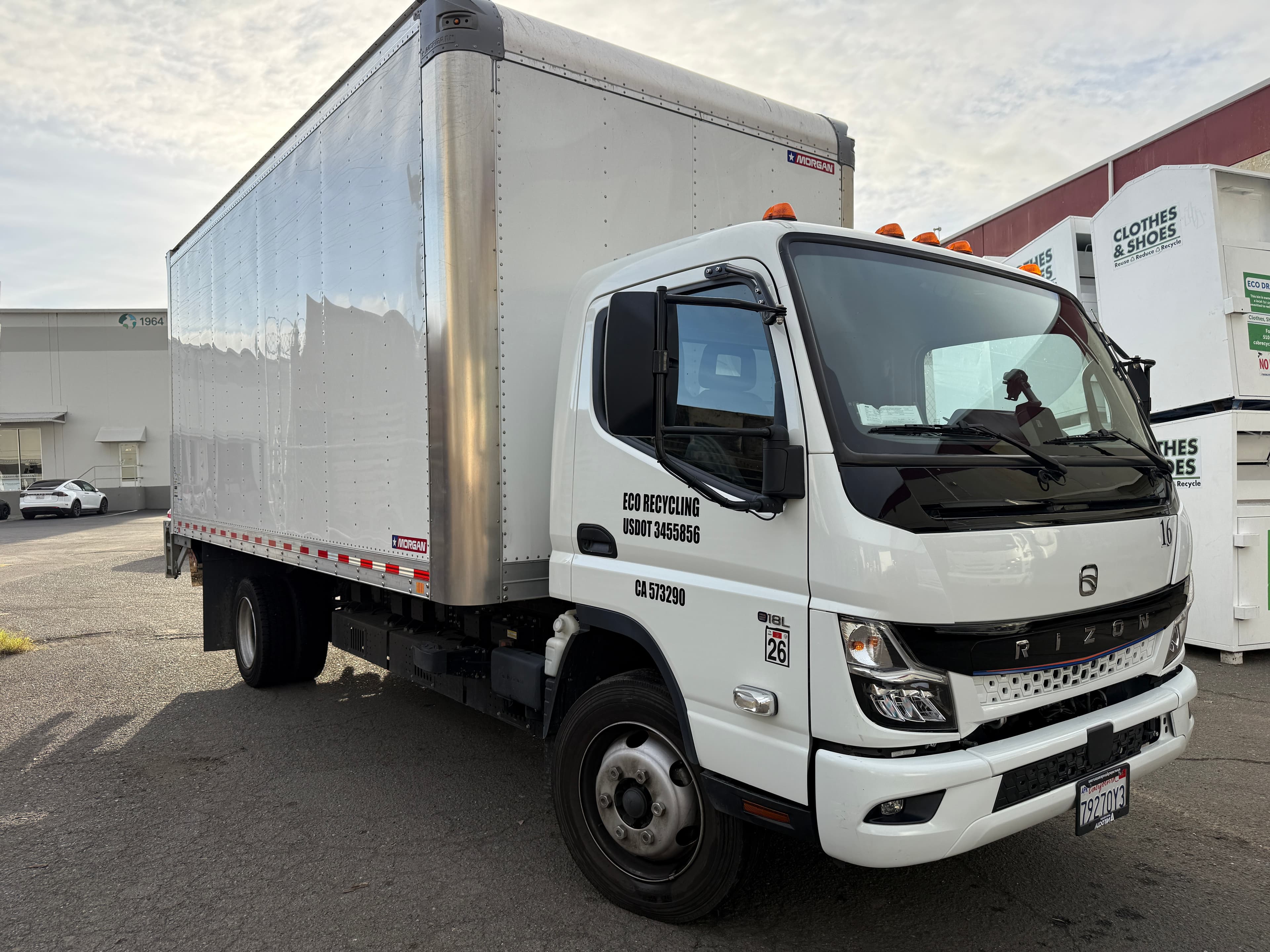White Eco Recycling box truck parked near clothes and shoes recycling bins outdoors.